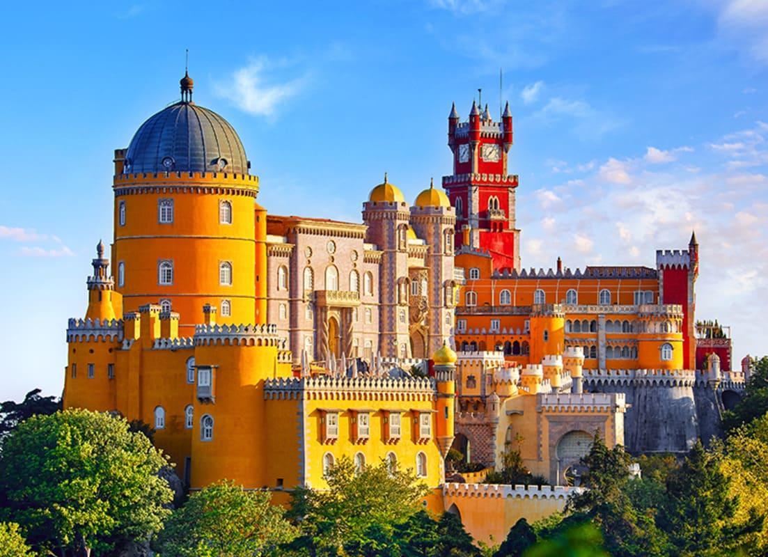 Palácio histórico amarelo e vermelho com cúpula azul e torre medieval sob céu azul claro.